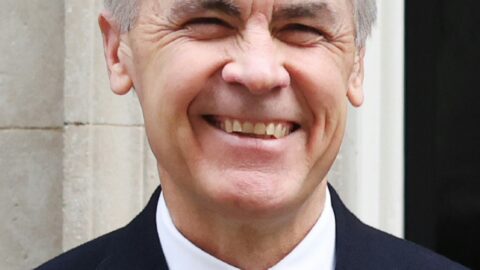 Canadian Prime Minister Mark Carney smiling in a suit with a poppy pin