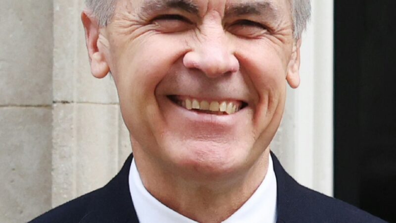Canadian Prime Minister Mark Carney smiling in a suit with a poppy pin