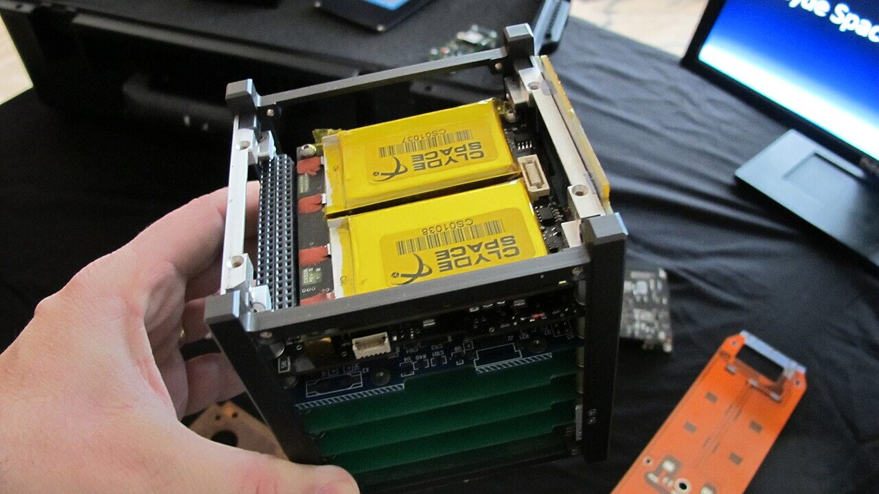 A small CubeSat satellite held in a hand during testing